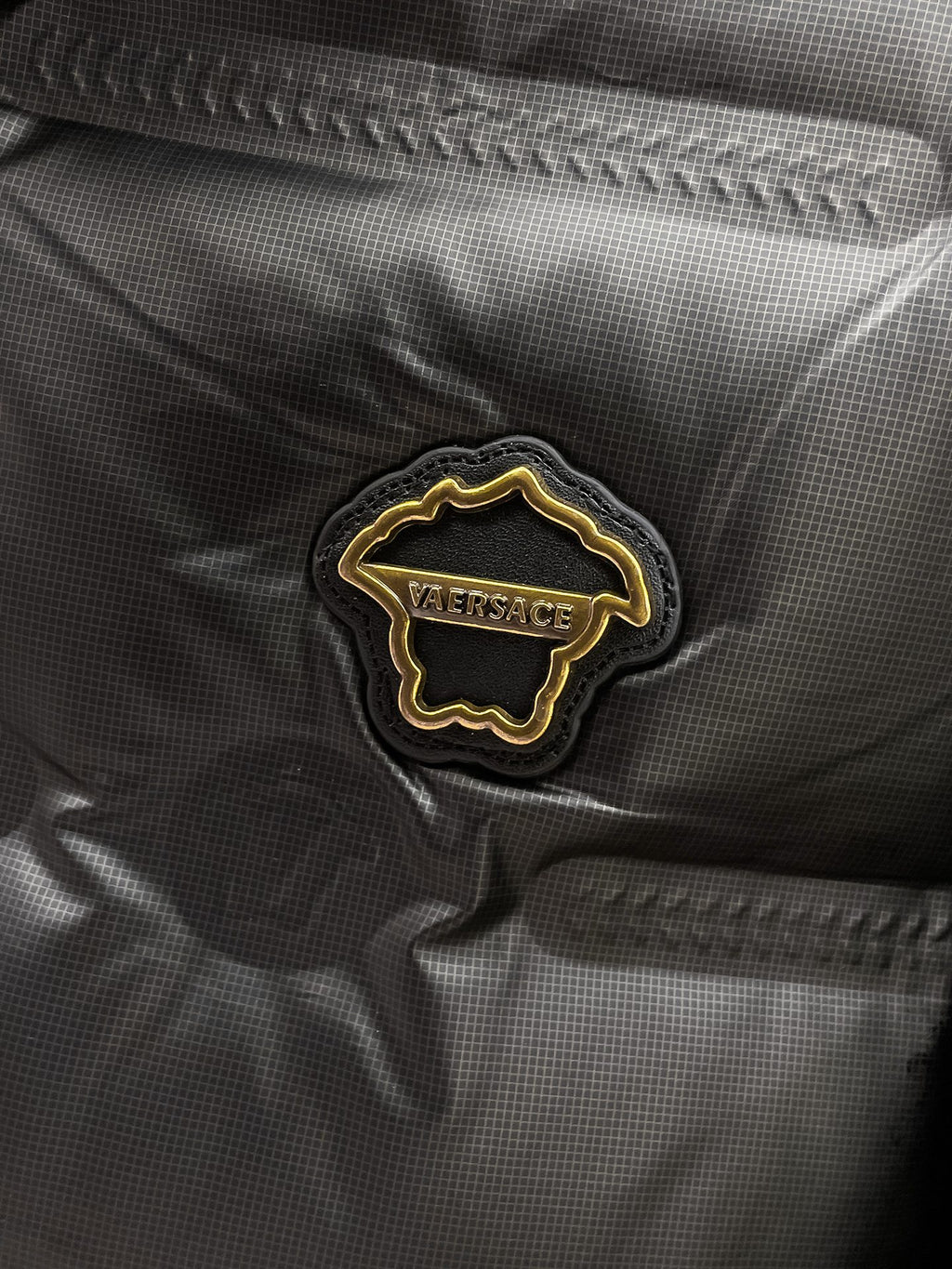 Black puffer jacket close-up of embroidered Versace logo patch