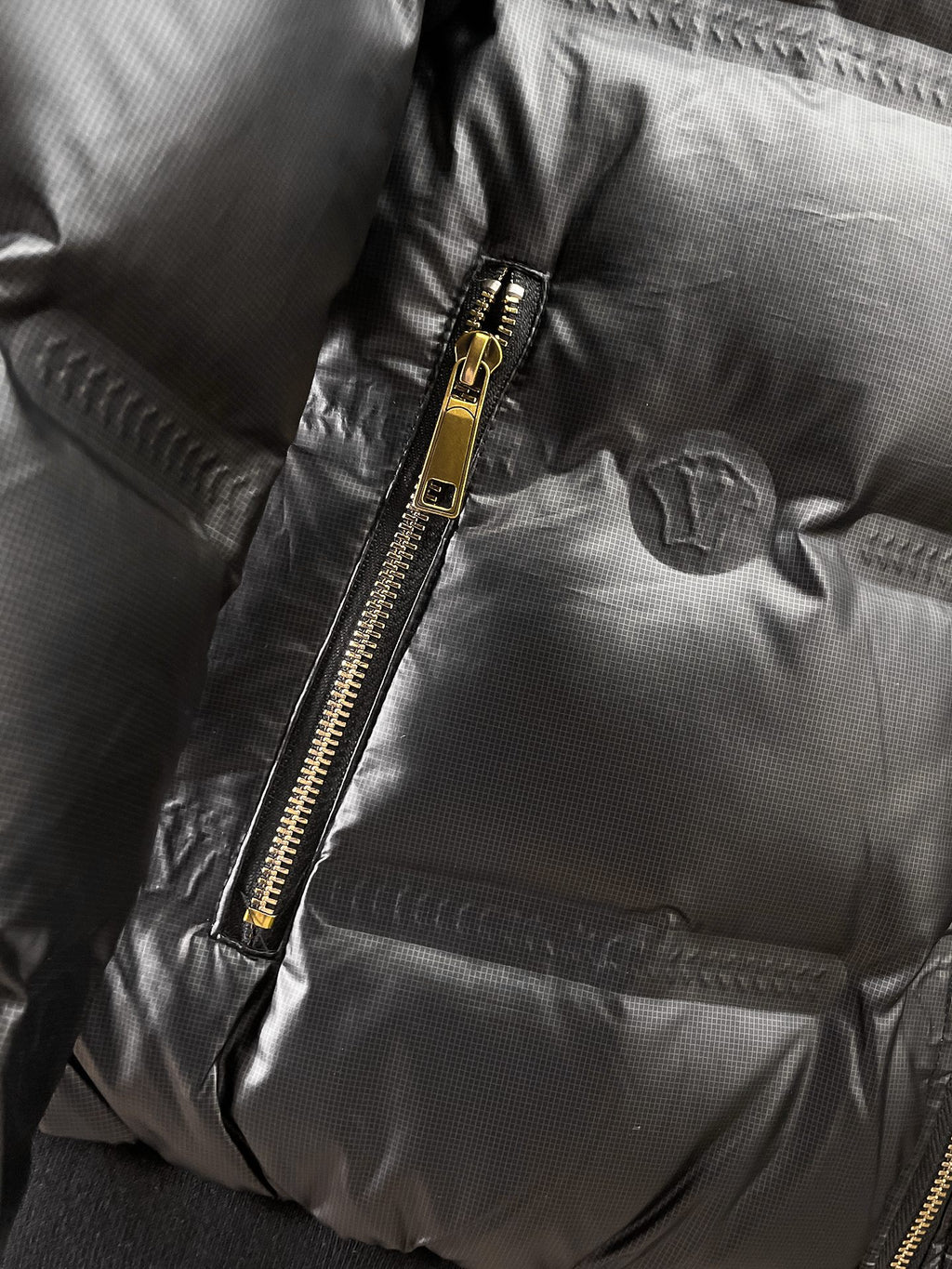 Black puffer jacket close-up of gold zipper and quilted front panel