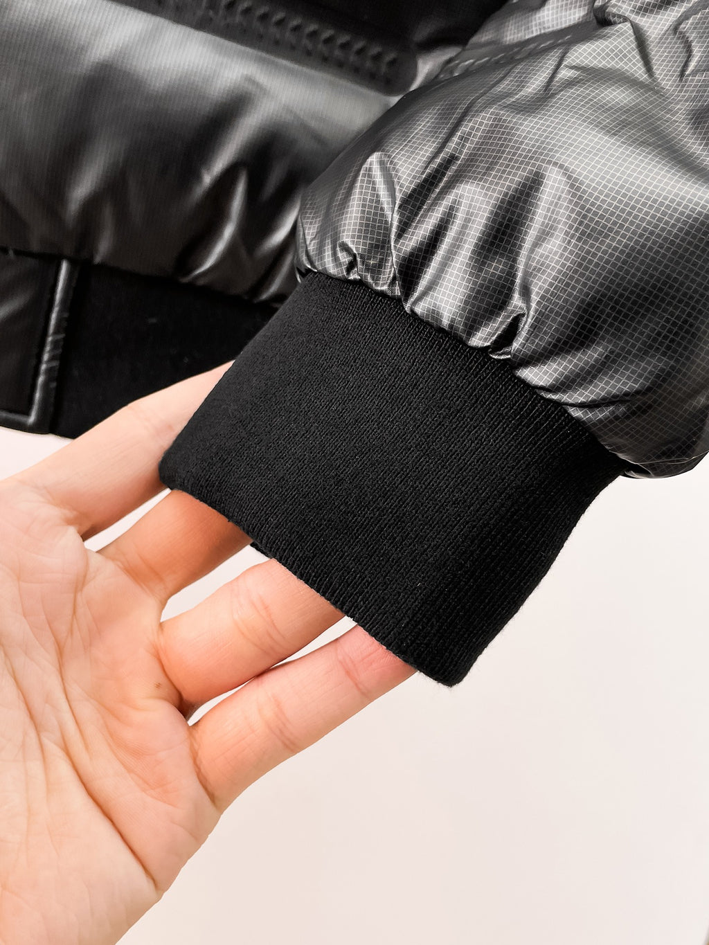 Black ribbed cuff on puffer jacket sleeve opening, shown in hand