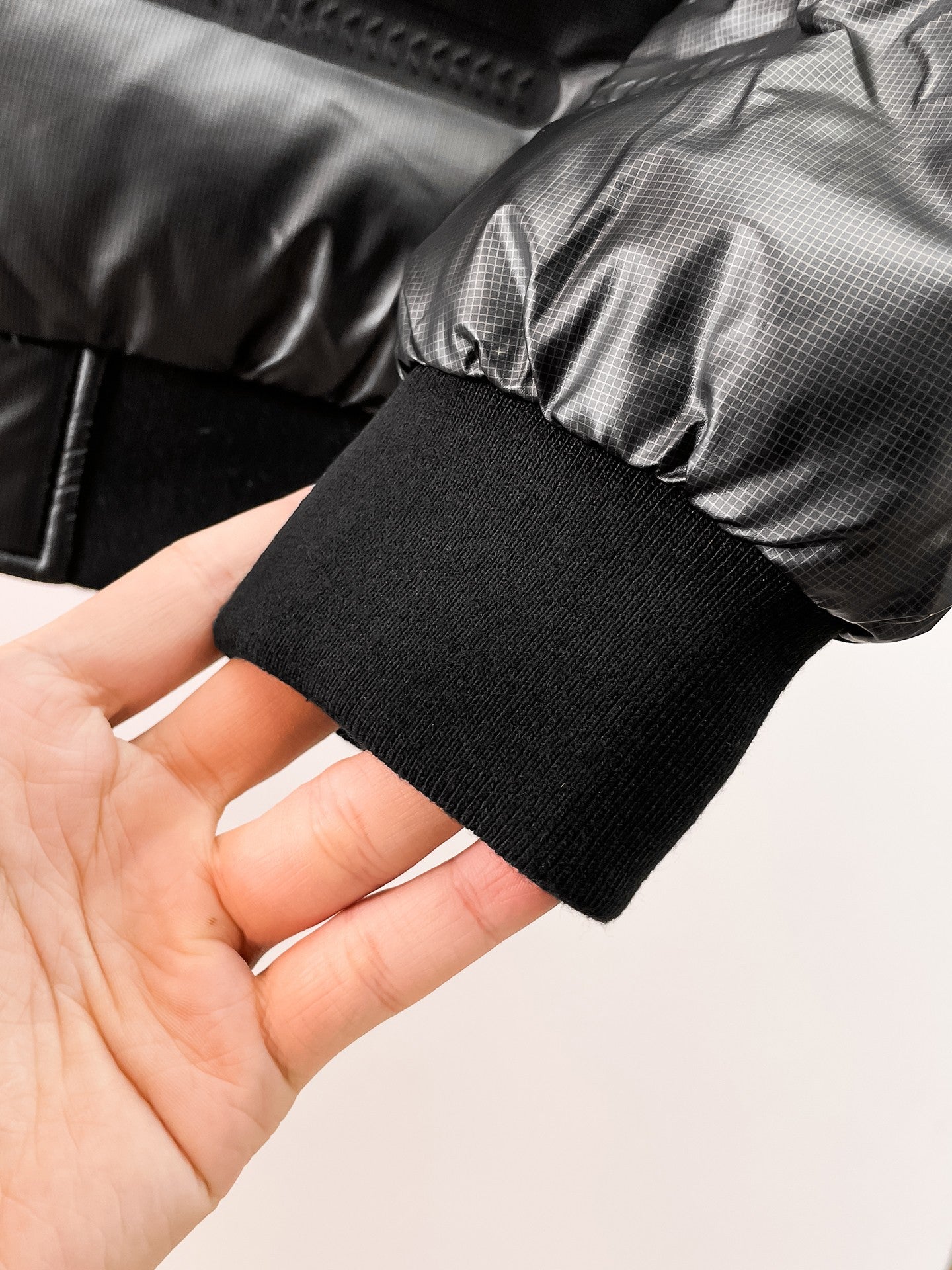 Black ribbed cuff on puffer jacket sleeve opening, shown in hand
