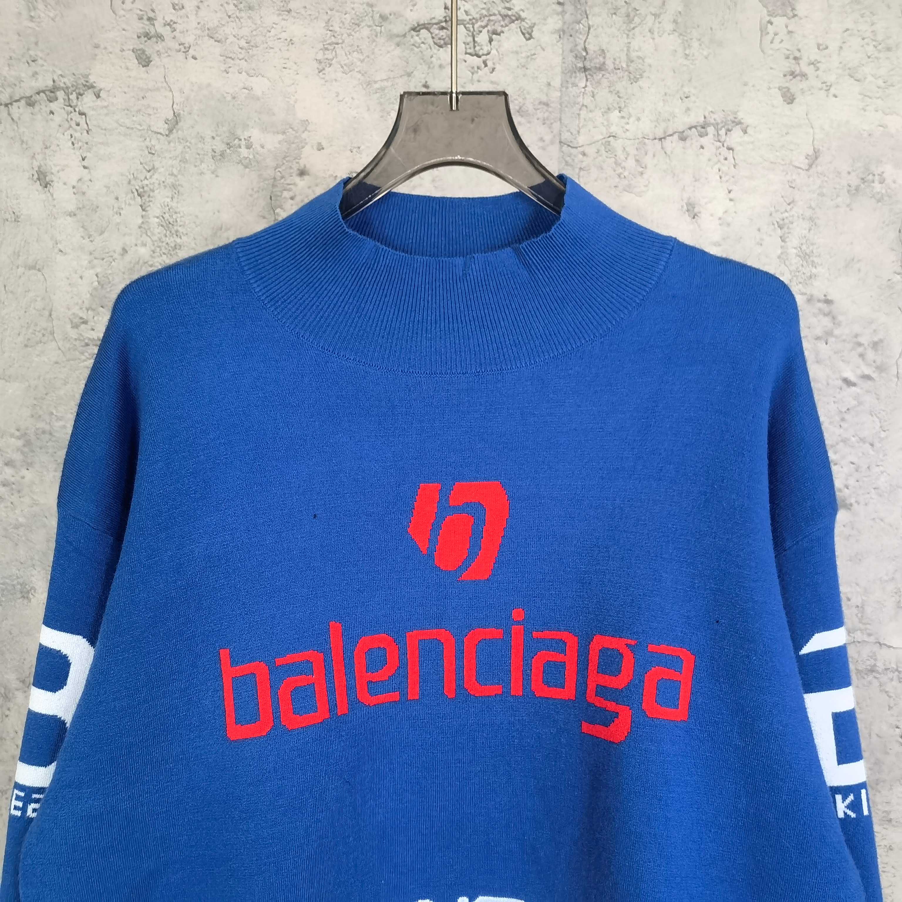 Blue sweater close-up with red balenciaga logo and white striped sleeve detail