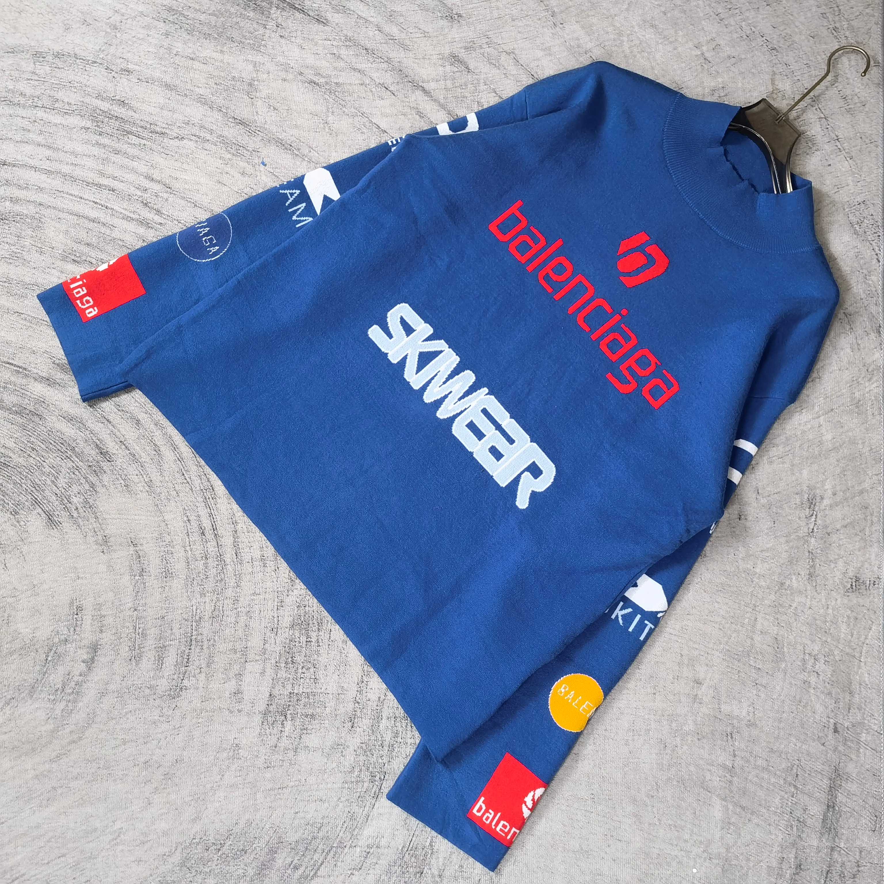 Blue long-sleeve sweater laid flat with SKWEAR graphic and red balenciaga logo