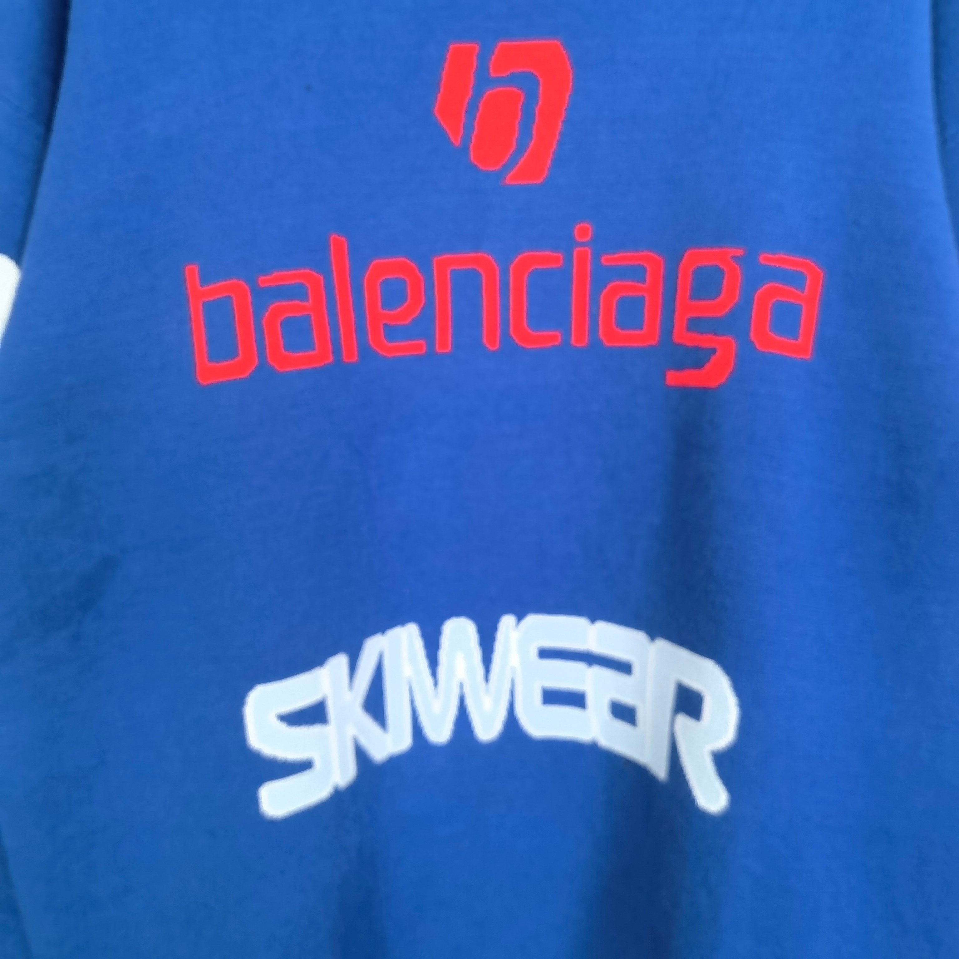 Blue sweater chest close-up with red balenciaga logo and white SKWEAR graphic