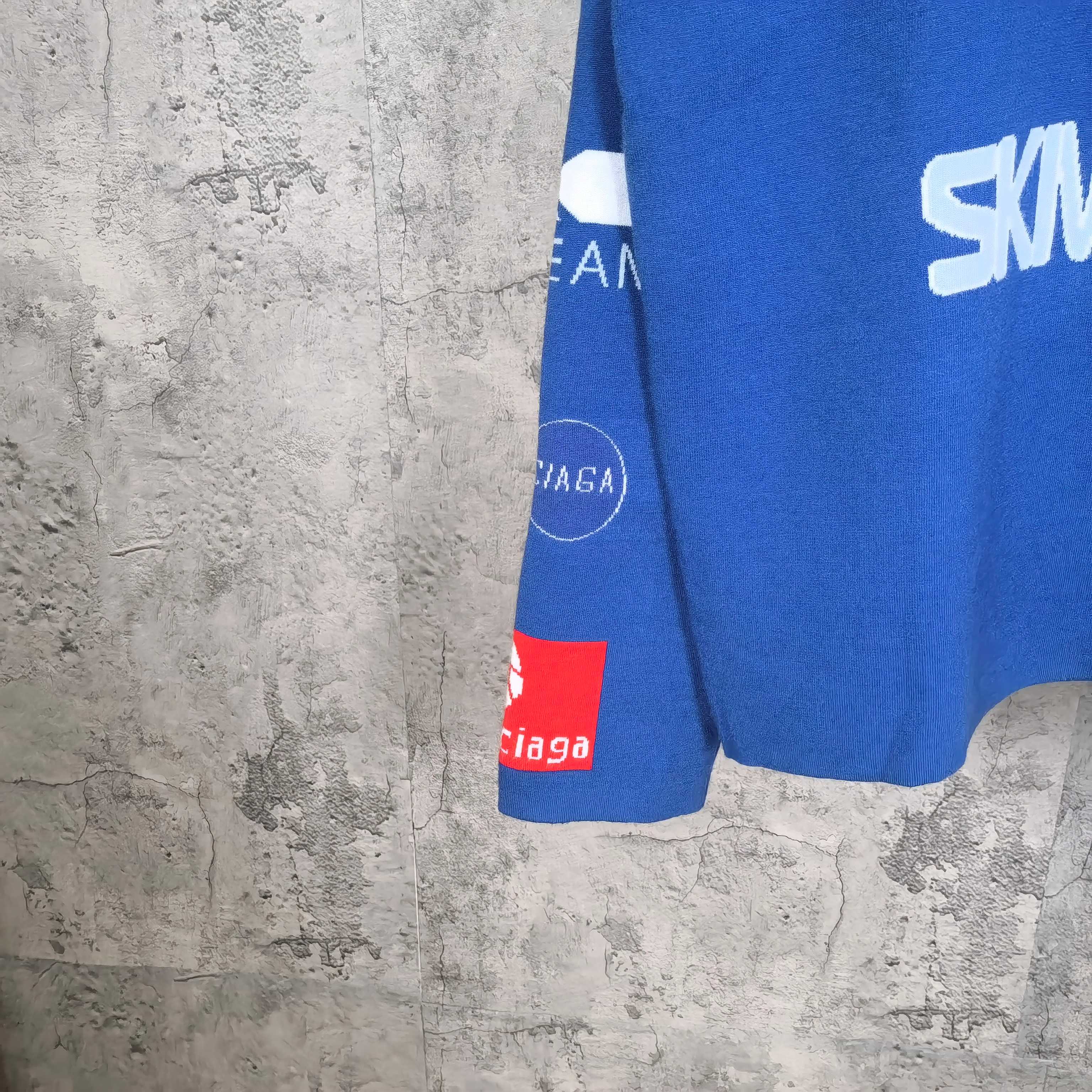 Blue sweater hem with red and white logo label and striped sleeve cuff