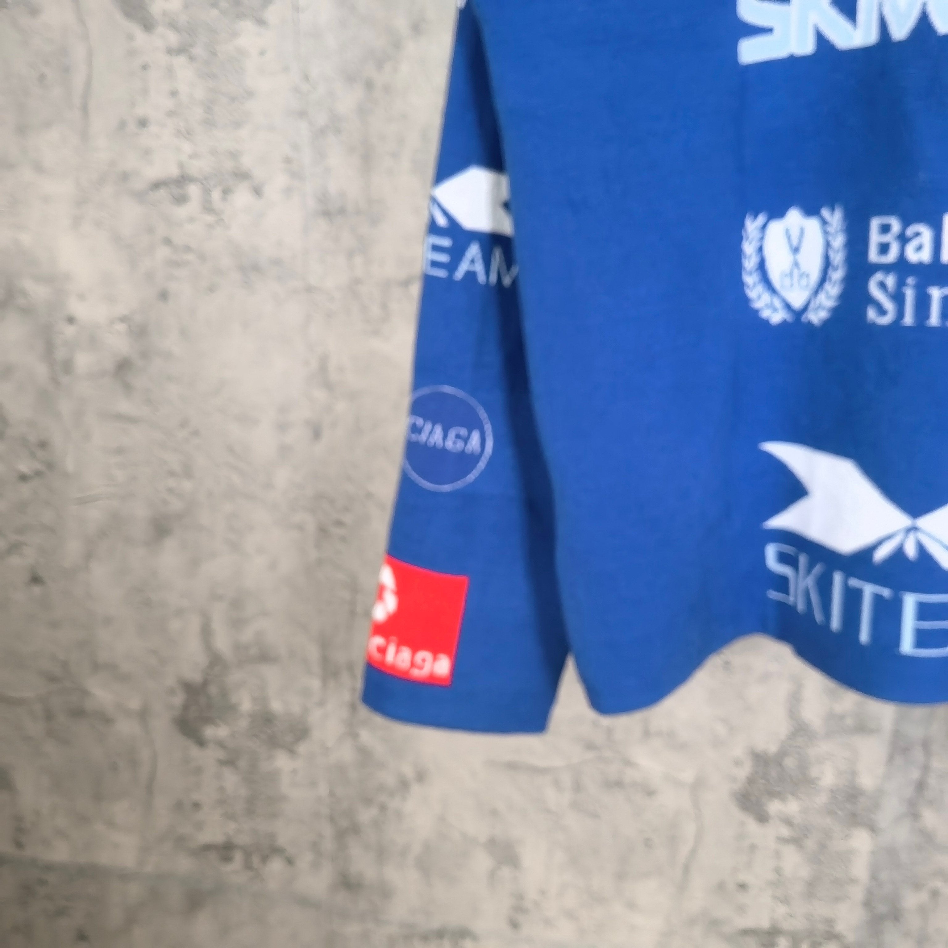 Blue long-sleeve shirt with side logos and multicolor graphic patch on sleeve