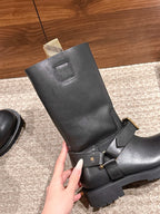 Black mid-calf boot held up, showing square toe, front strap and buckle.