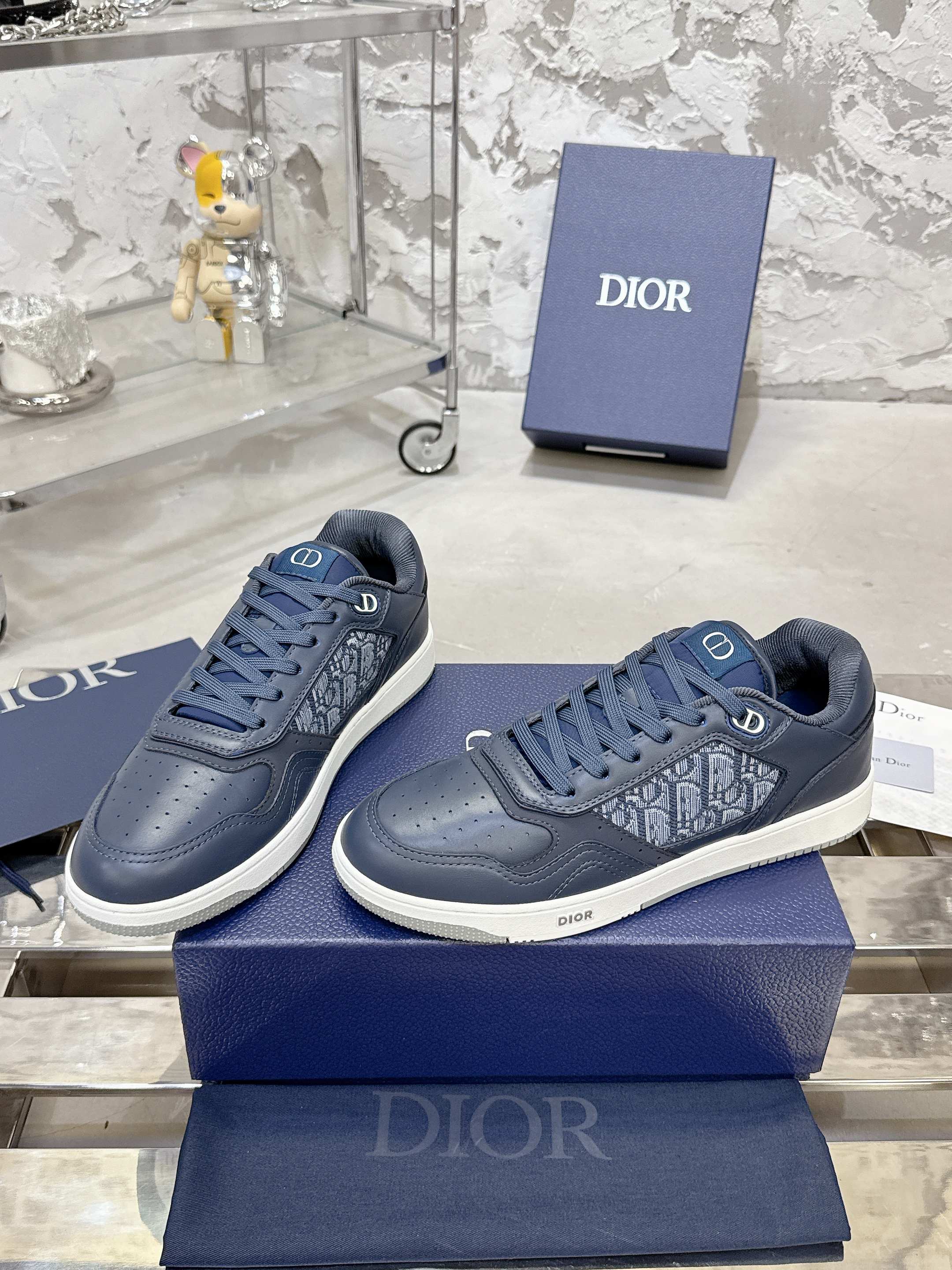 Pair of unisex low-top sneakers in dark blue with lace-up front and white soles on boxes