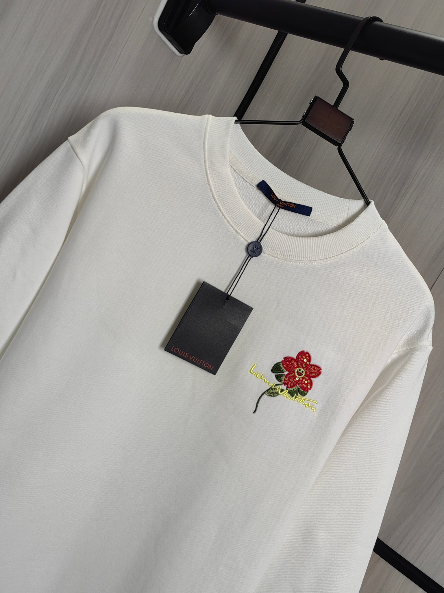 White crewneck sweatshirt detail with red flower embroidery and hanging size tag