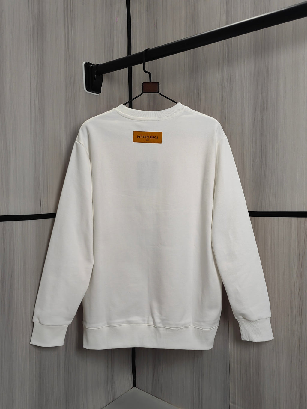 White crewneck sweatshirt back view on hanger with small orange label