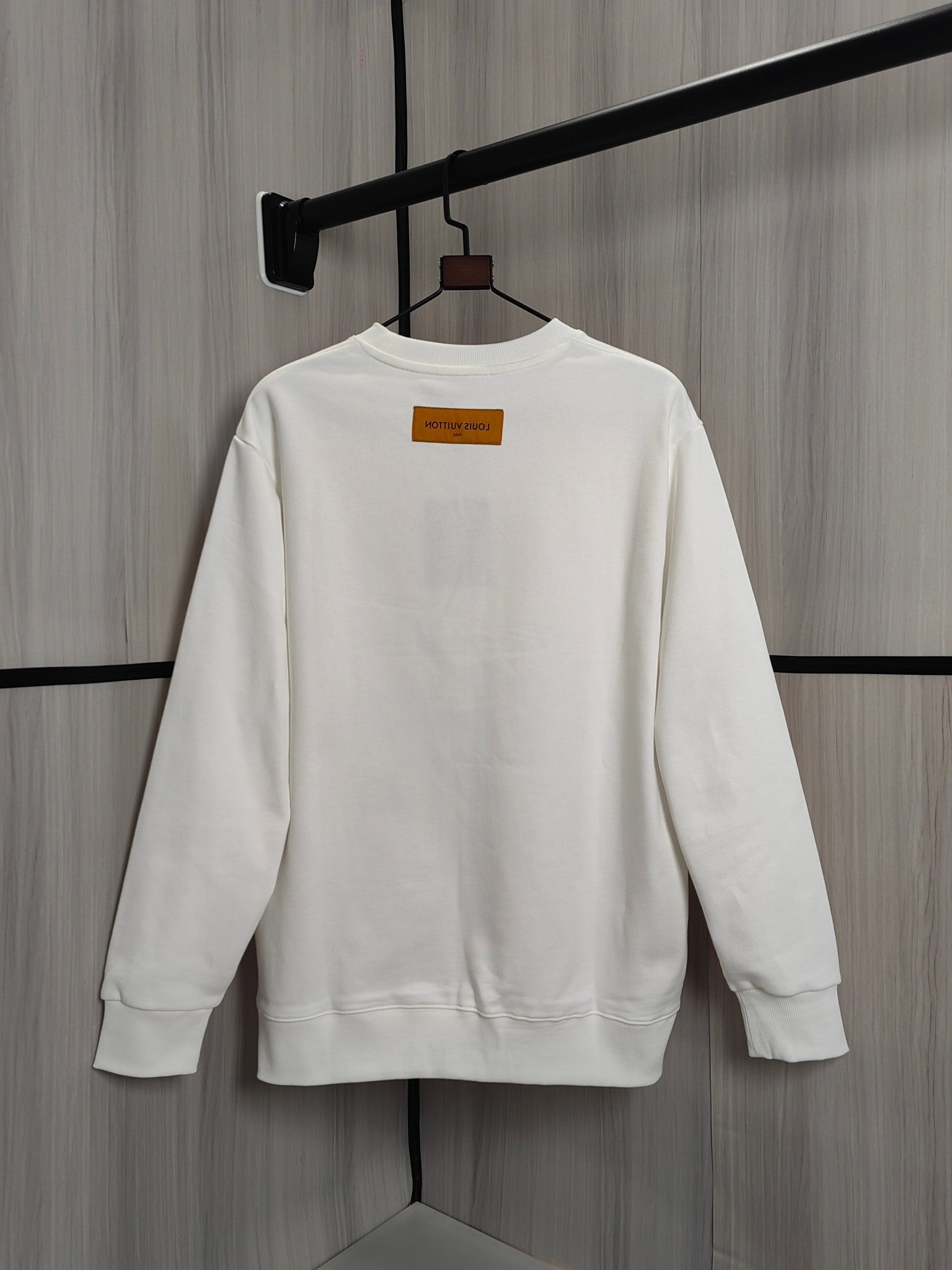 White crewneck sweatshirt back view on hanger with small orange label
