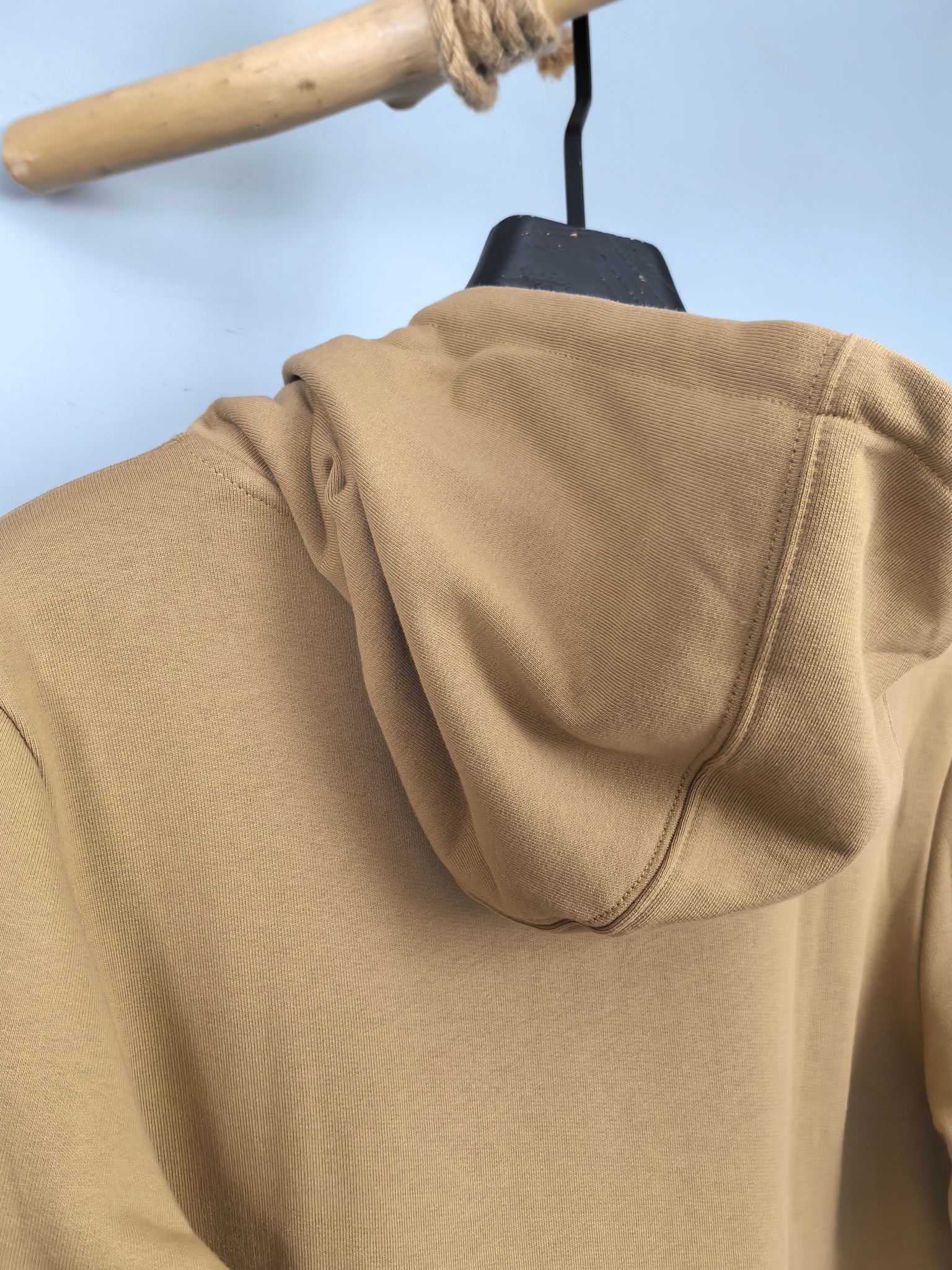 Tan hoodie back with hood and zipper seam, close-up on hanger
