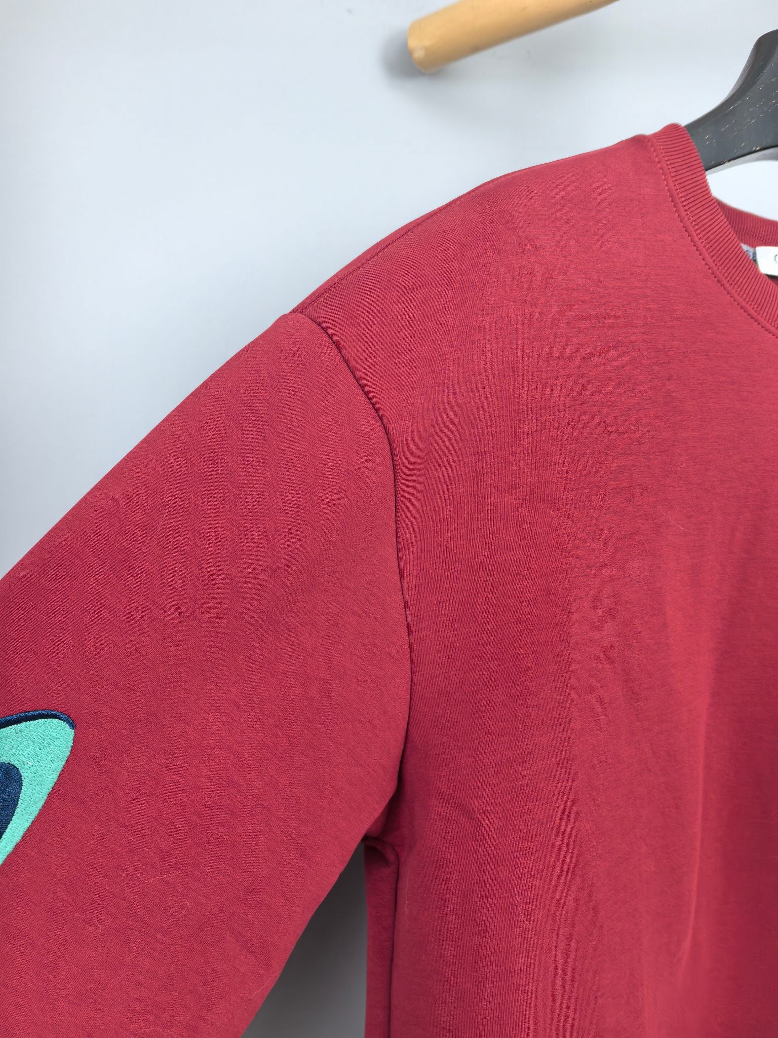 Red long-sleeve sweatshirt sleeve with partial turquoise graphic