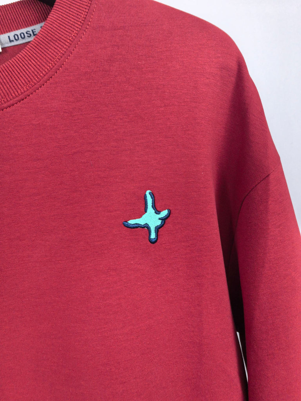 Red long-sleeve sweatshirt with small turquoise cross logo