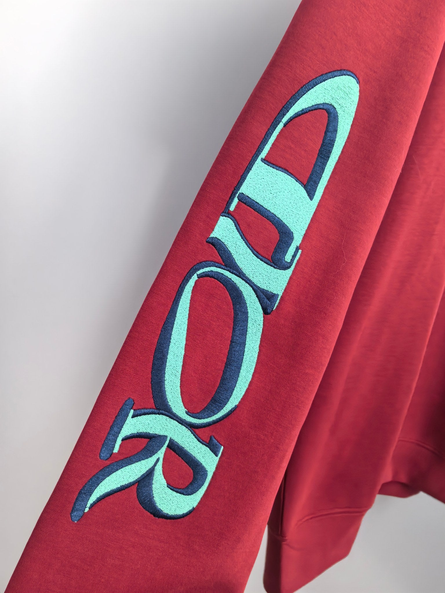 Red sweatshirt sleeve with large turquoise graphic lettering