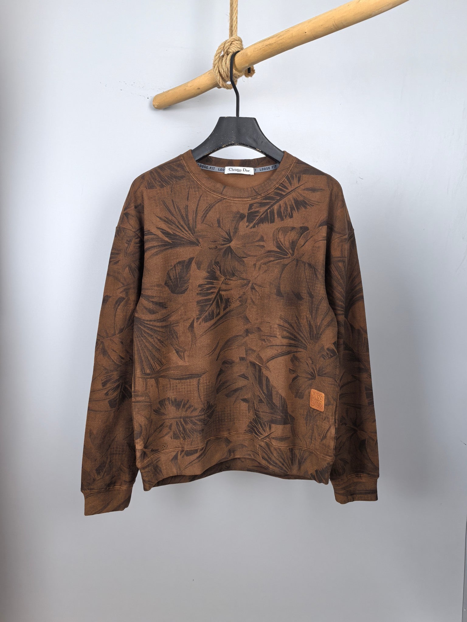 Brown long-sleeve top with dark leaf print, crew neck and small front pocket detail