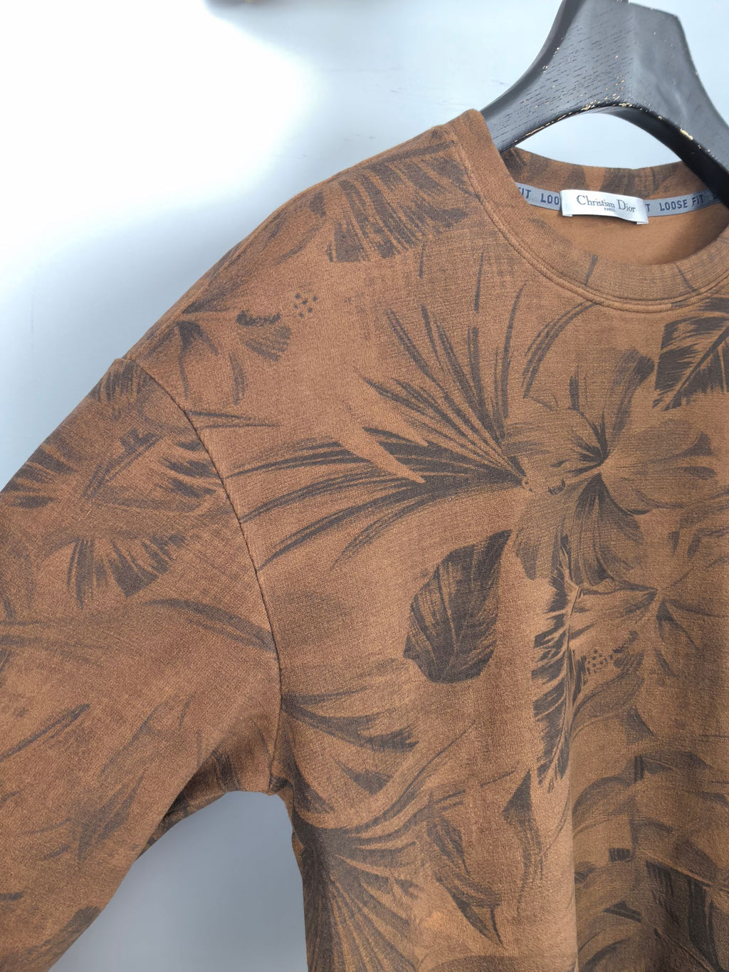 Brown long-sleeve top with dark tropical leaf print, close-up of sleeve and shoulder
