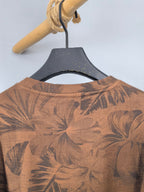 Back view of brown long-sleeve top with dark tropical leaf print and crew neck