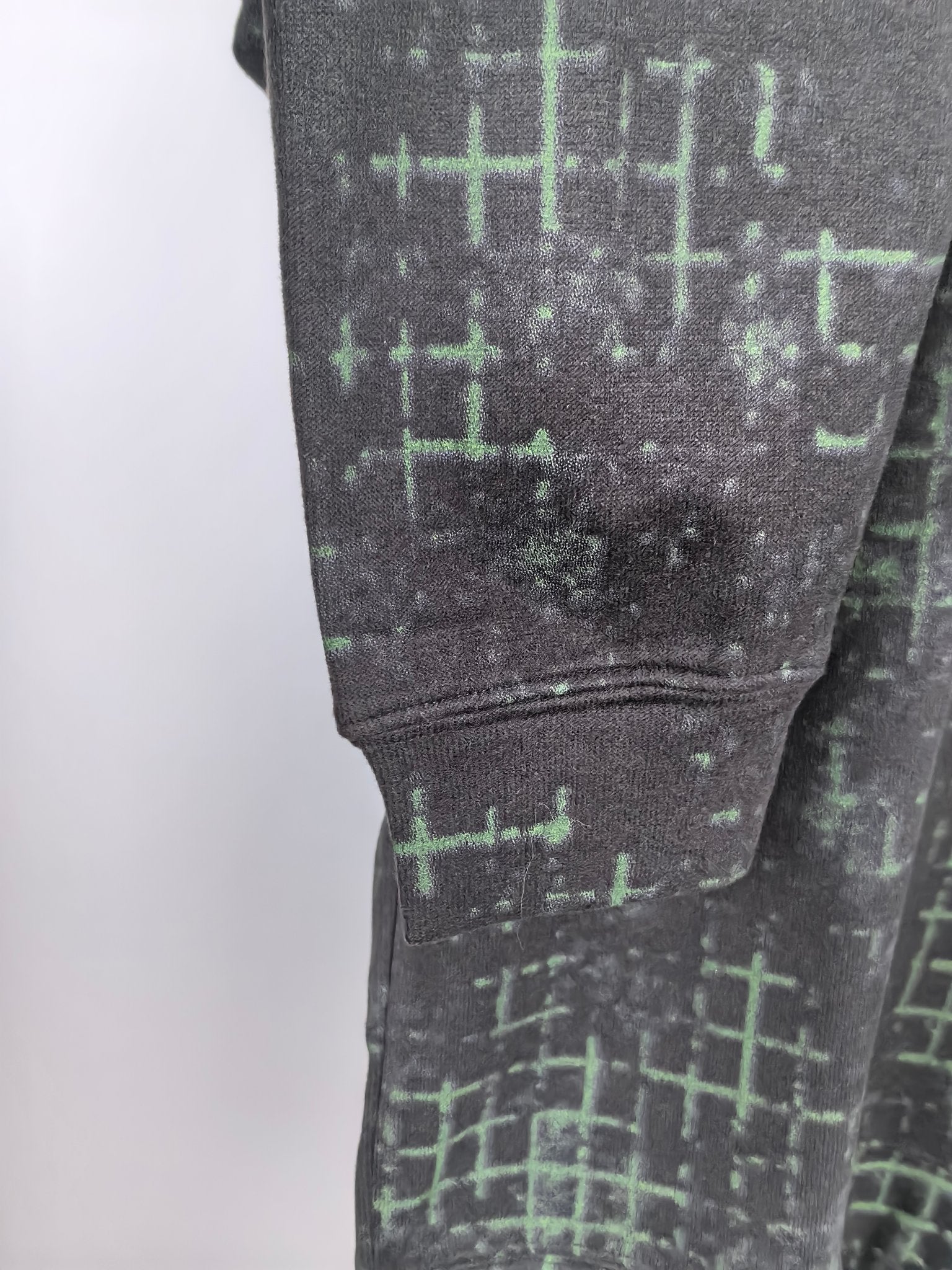 Black sweatshirt sleeve cuff with green grid pattern and ribbed cuff detail