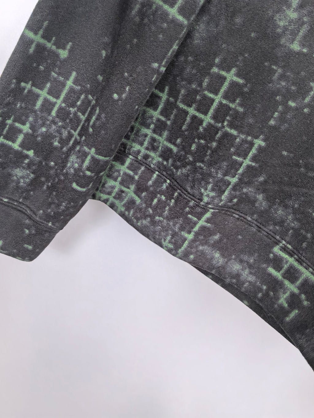 Black sweatshirt side seam with green grid pattern and ribbed cuff edge