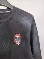 Long-sleeve crewneck shirt with circular red-and-white chest patch, dark charcoal fabric