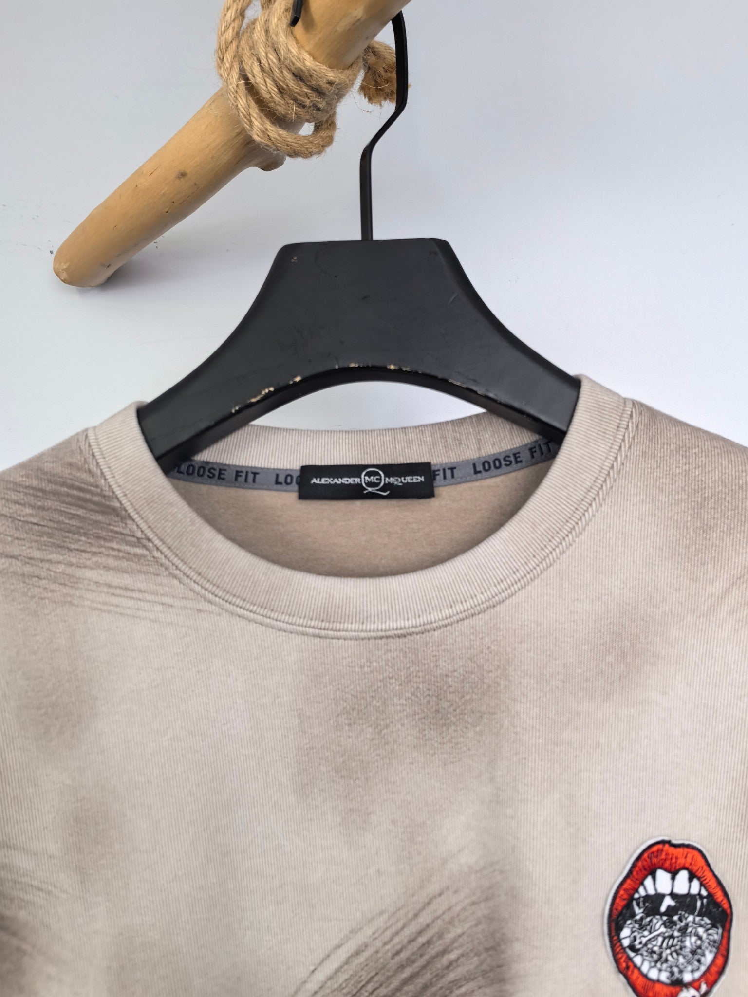 Light beige crewneck sweatshirt collar with interior label and red chest graphic.