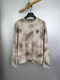 Light beige long-sleeve crewneck sweatshirt with small chest graphic patch.