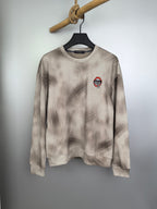 Light beige long-sleeve crewneck sweatshirt with small chest graphic patch.