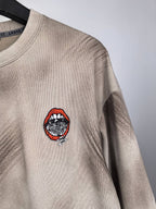 Light beige sweatshirt with red and black circular chest graphic patch.