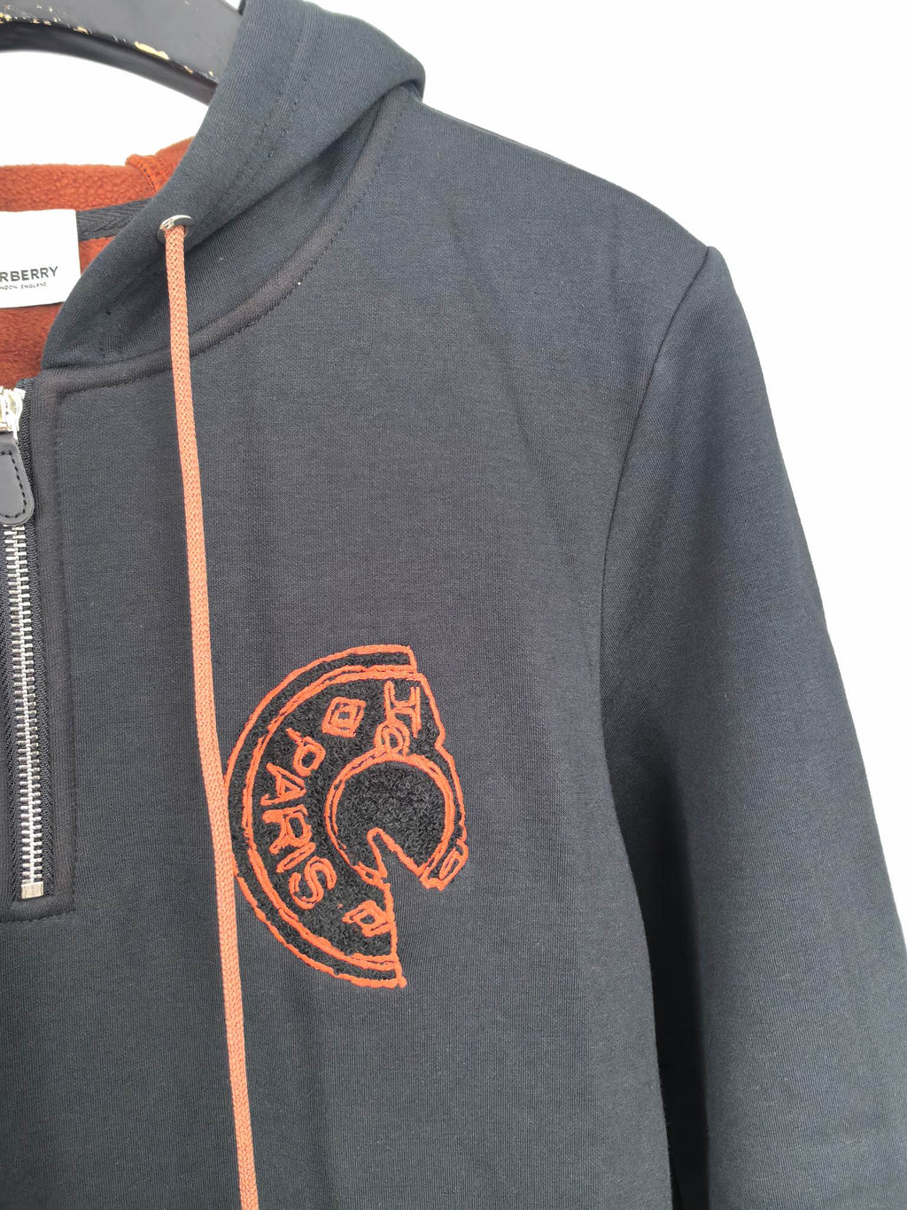 Dark gray hoodie sleeve with orange embroidered Burberry logo emblem