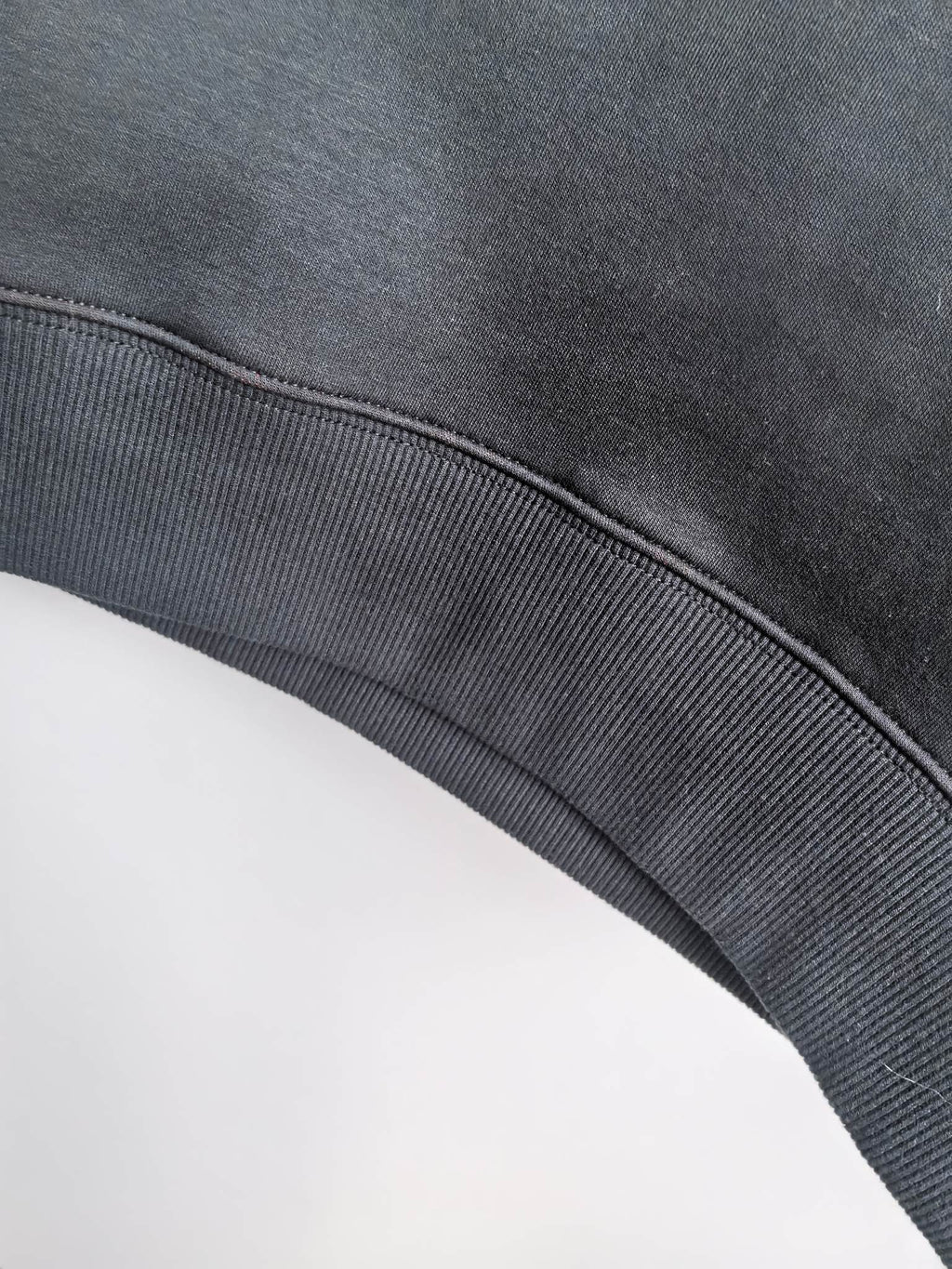 Dark gray hoodie waistband with ribbed knit trim and curved hem