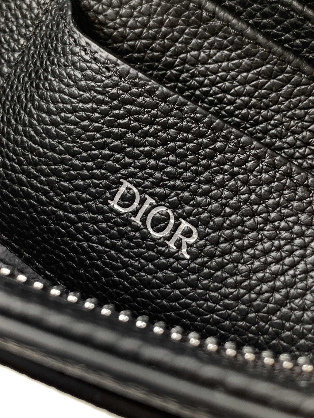 Dior bag with embossed Dior logo on dark pebbled leather and stitched edge.