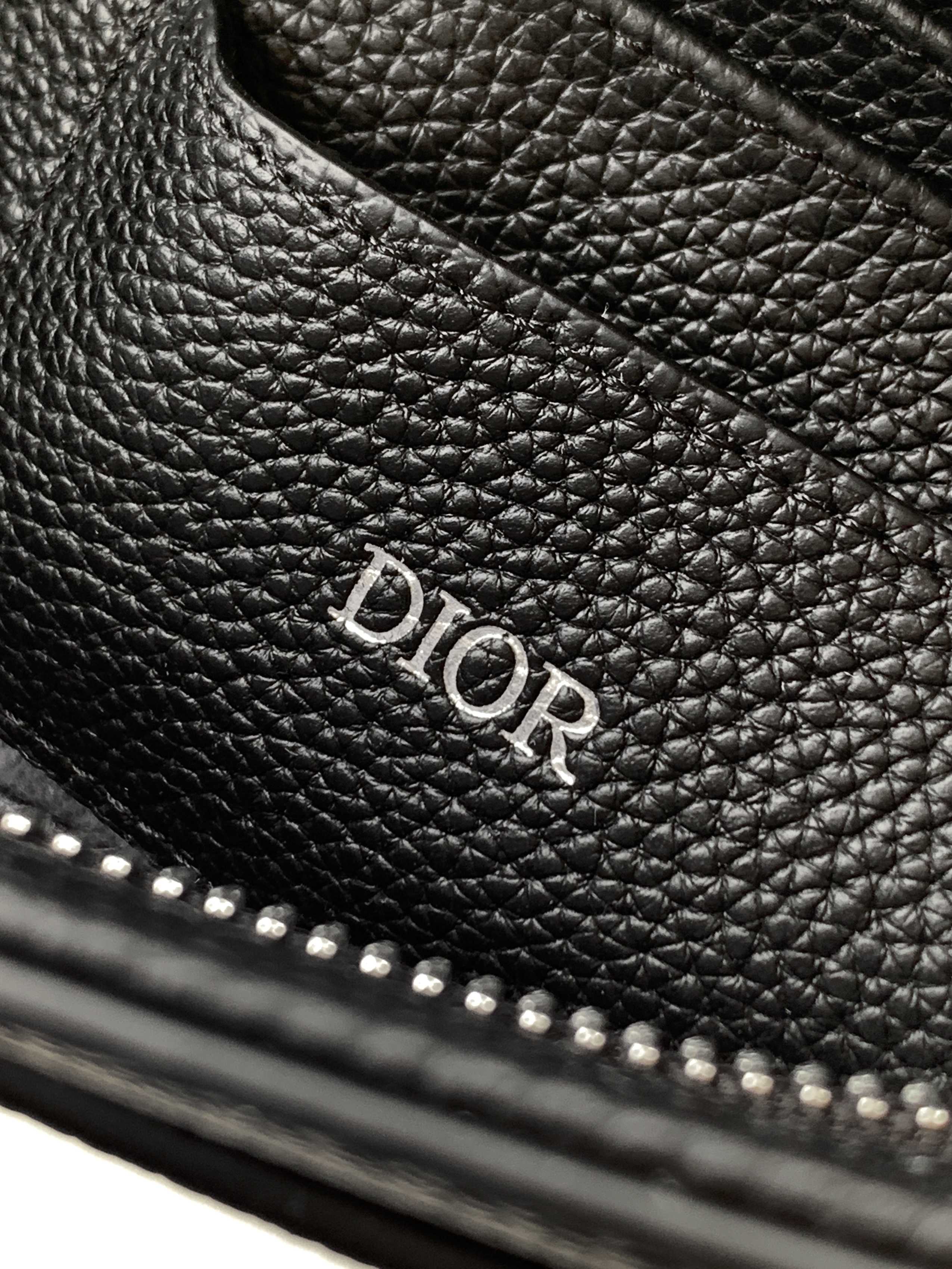 Dior bag with embossed Dior logo on dark pebbled leather and stitched edge.