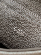 Dior men’s bag close-up of “Dior” logo stamped on textured dark leather