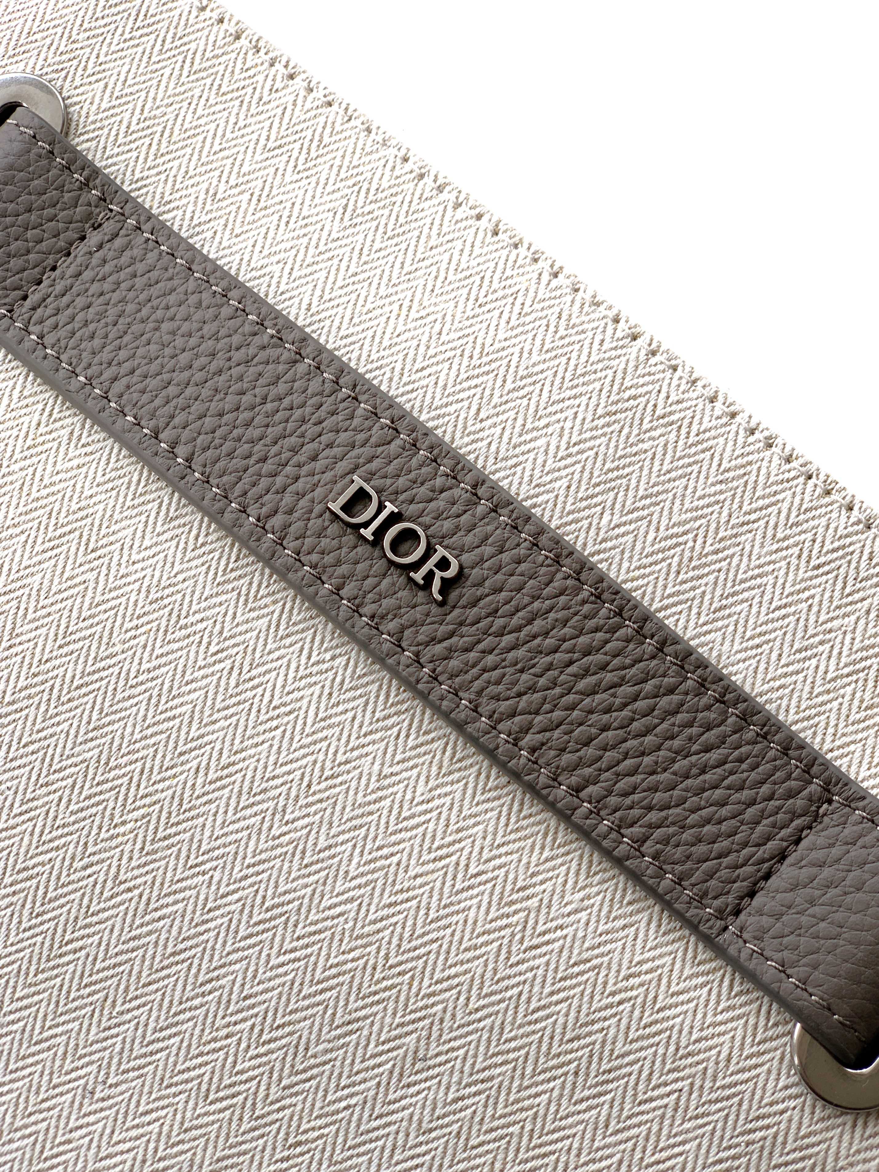 Dior men’s bag close-up of “Dior” logo on dark leather trim along the edge