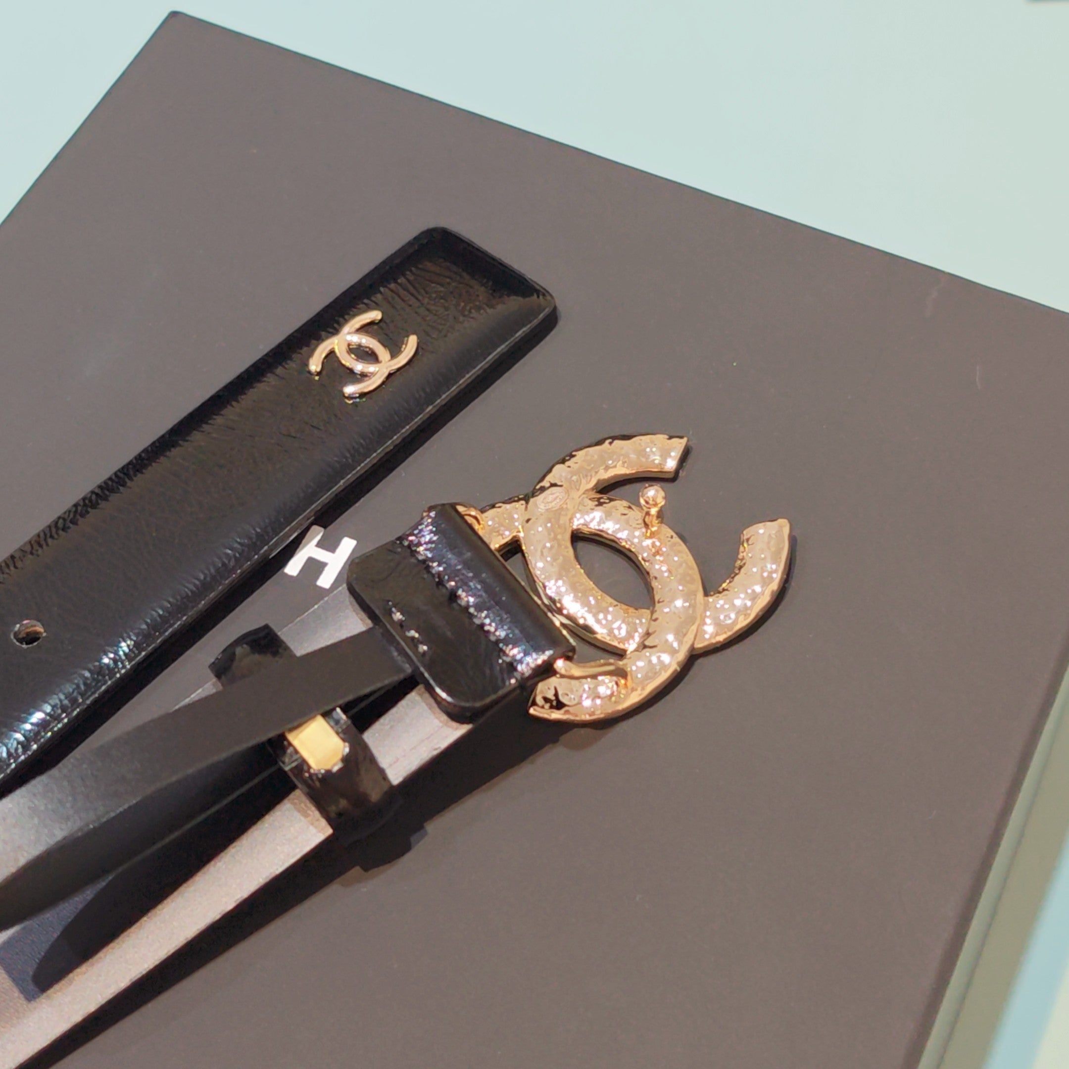 Chanel belt close-up with black leather strap, gold-tone double C buckle and CC charm