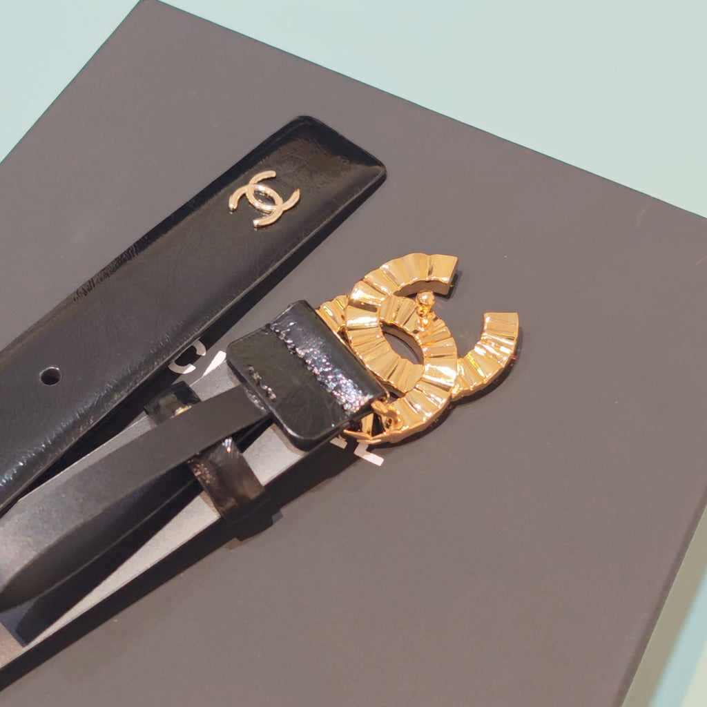 Chanel belt close-up of gold-tone CC buckle on dark leather strap atop box