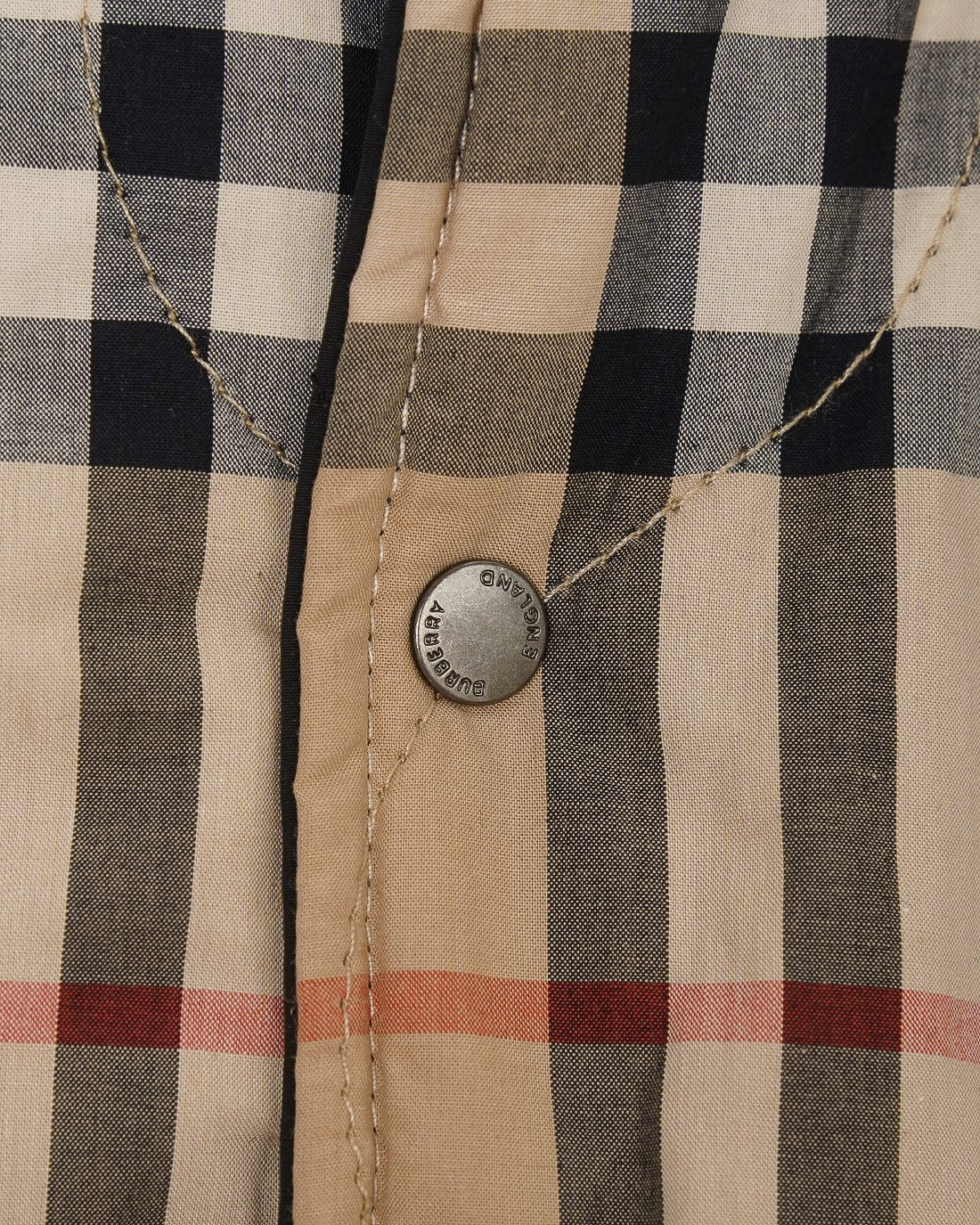 Plaid quilted jacket button detail on beige and black check fabric with visible stitching.