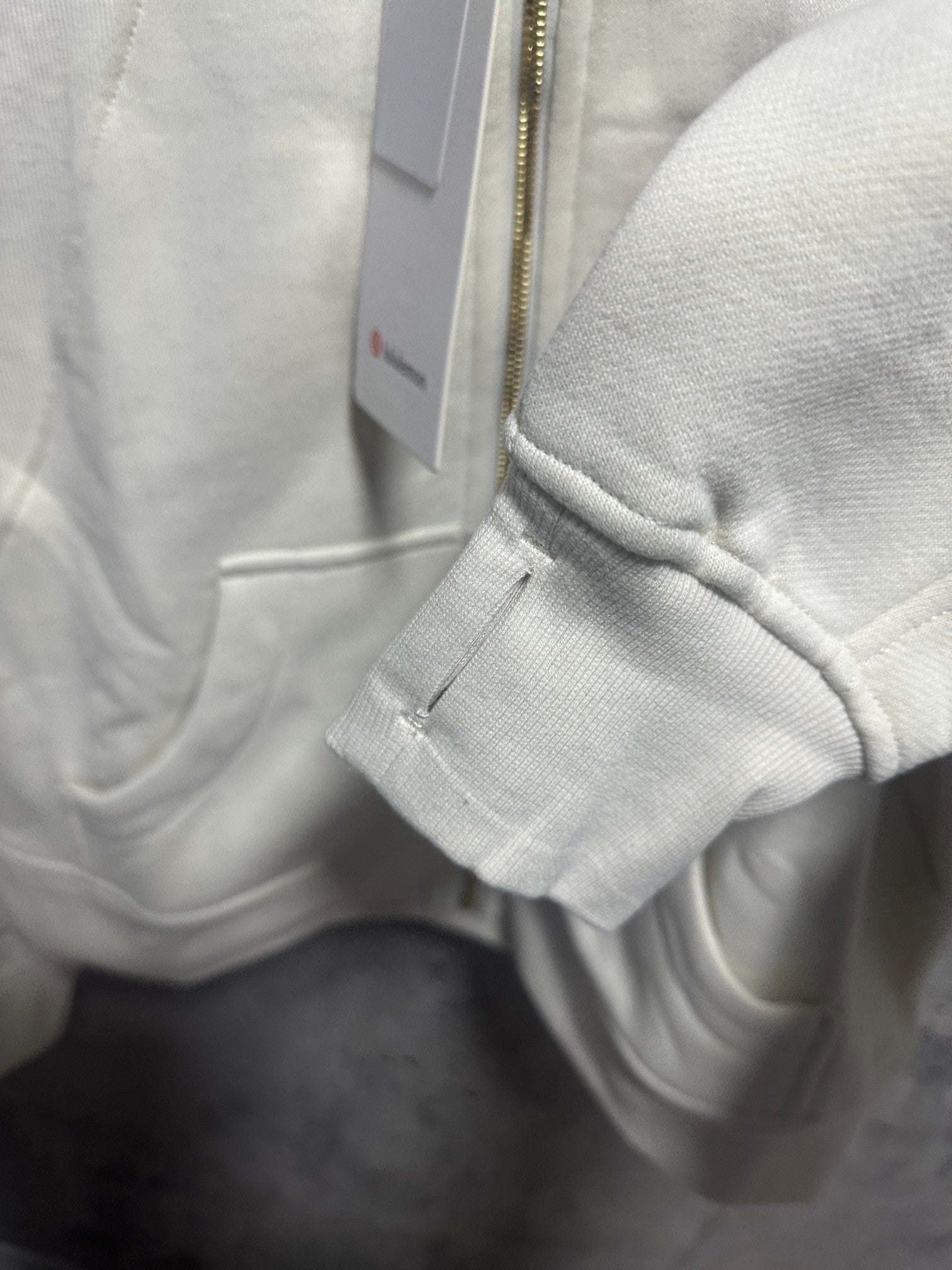 Cream zip-up hoodie sleeve cuff and small tag near zipper