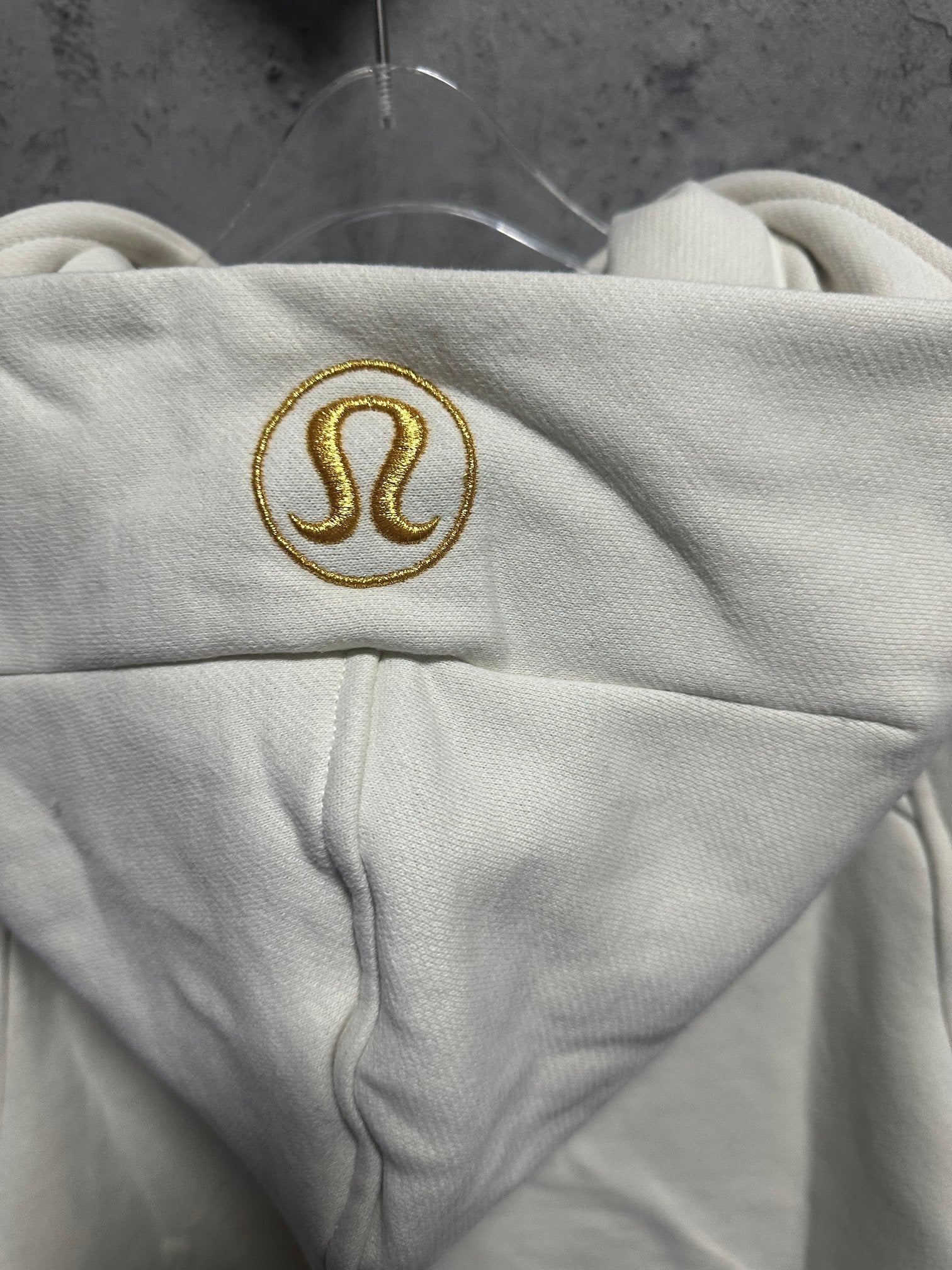 Off-white hoodie with embroidered gold omega-style logo on the hood panel