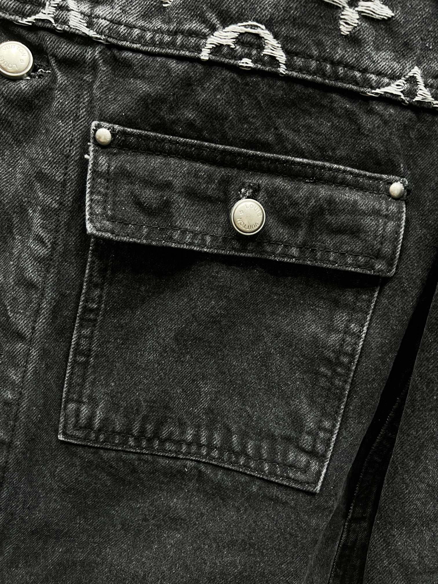 Black denim jacket chest flap pocket with gold-tone button and stitched panel detail