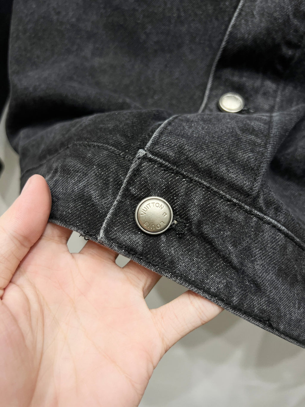 Black denim jacket cuff with gold-tone button and contrast stitching