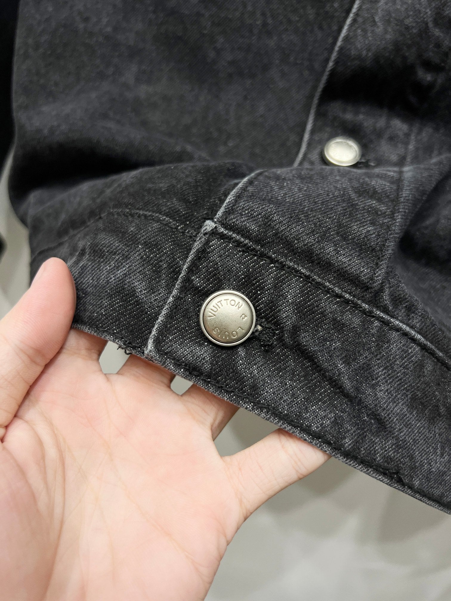 Black denim jacket cuff with gold-tone button and contrast stitching