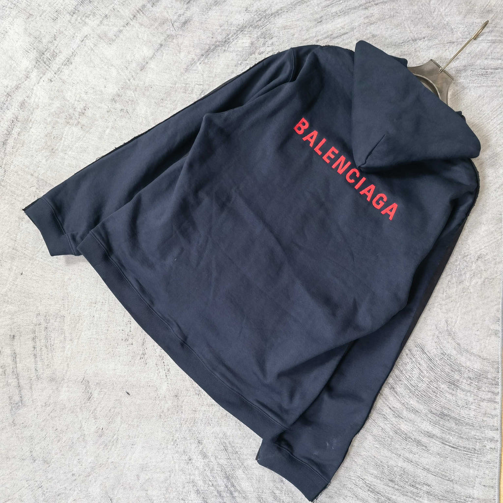 Navy hooded jacket with red BALENCIAGA logo on the back, laid flat.