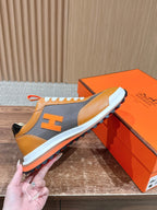 Hermes sneaker held by hand, orange leather, gray side panels, white laces