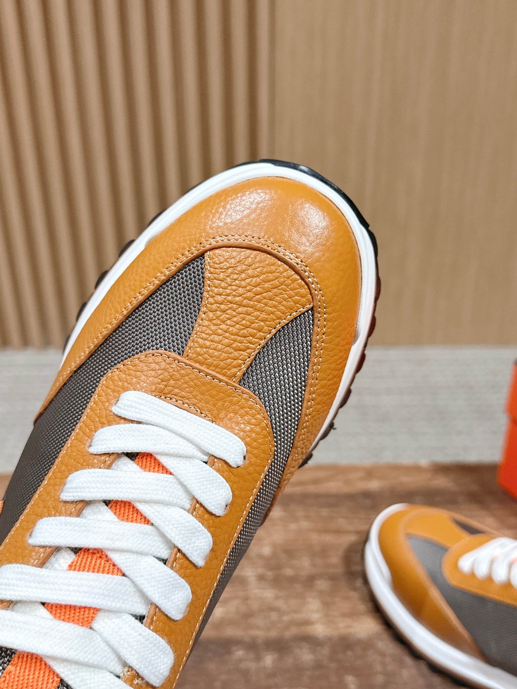 Hermes sneaker close-up, orange leather toe with gray side panel and white laces