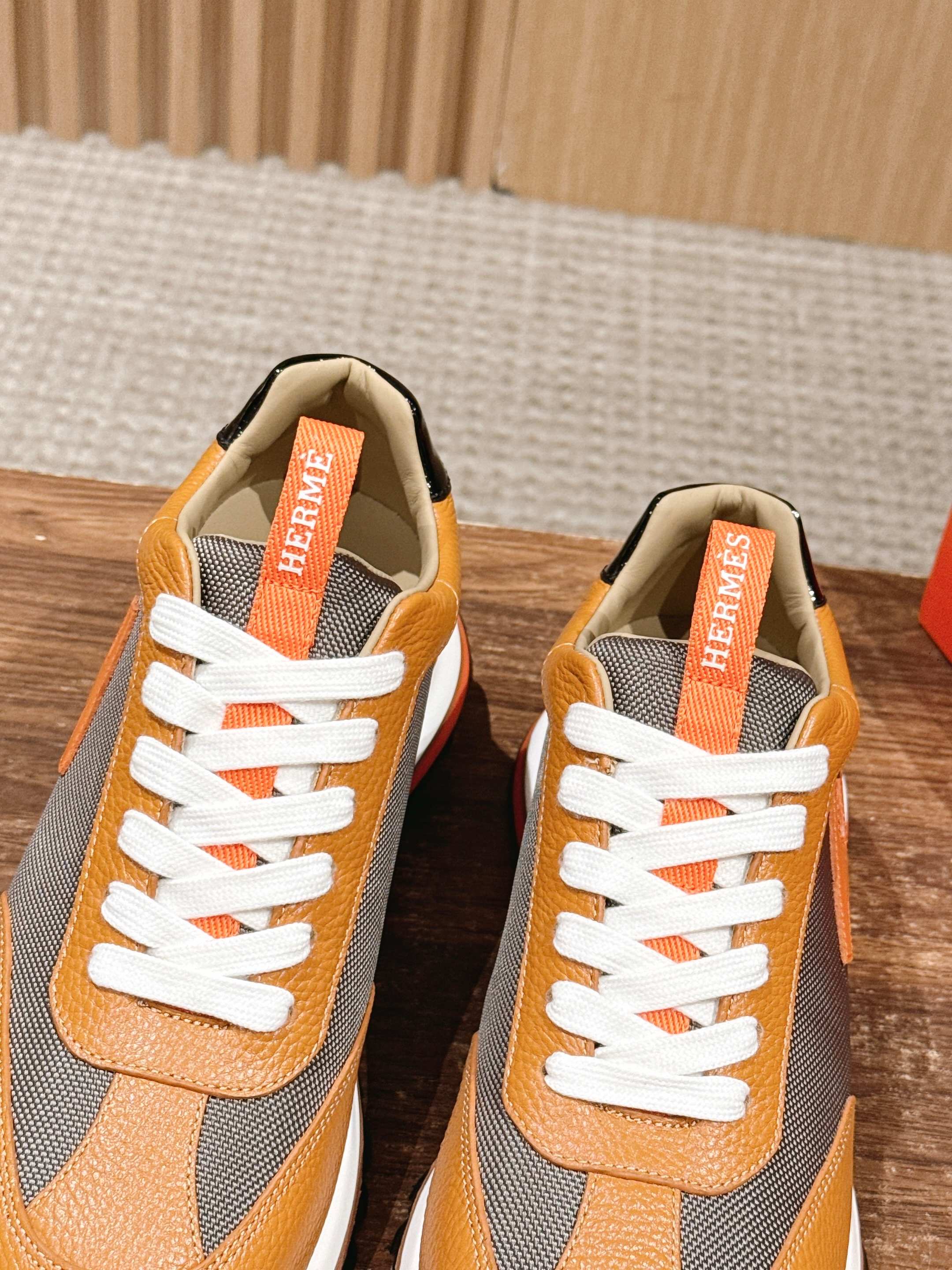Hermes sneakers pair, orange leather and gray panels with white laces and logo tags