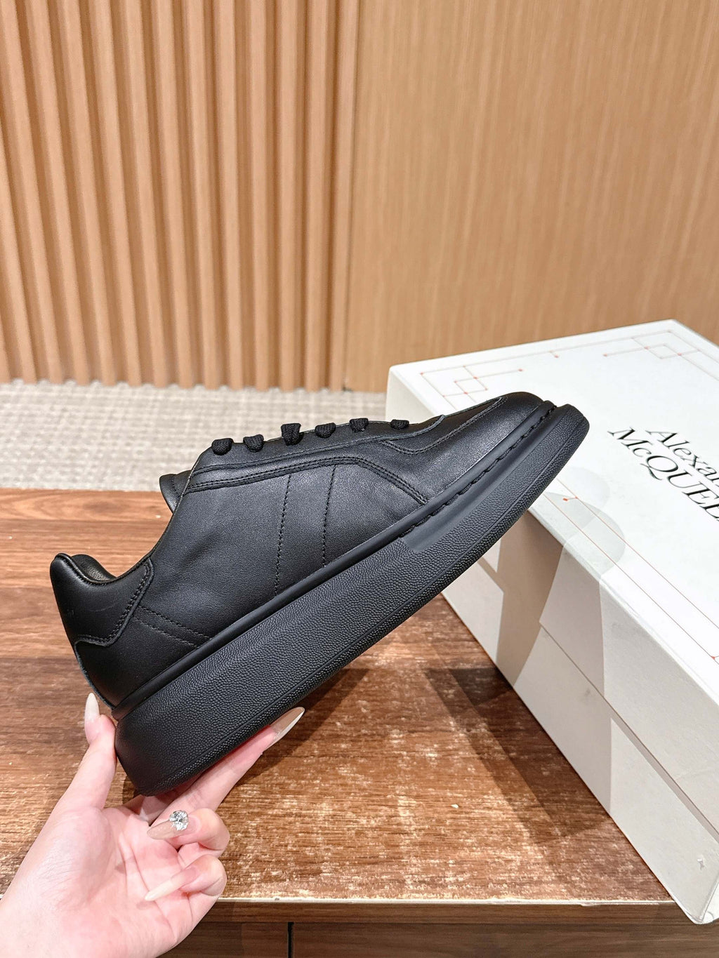 Black leather lace-up sneaker with rounded toe and rubber sole, held in hand