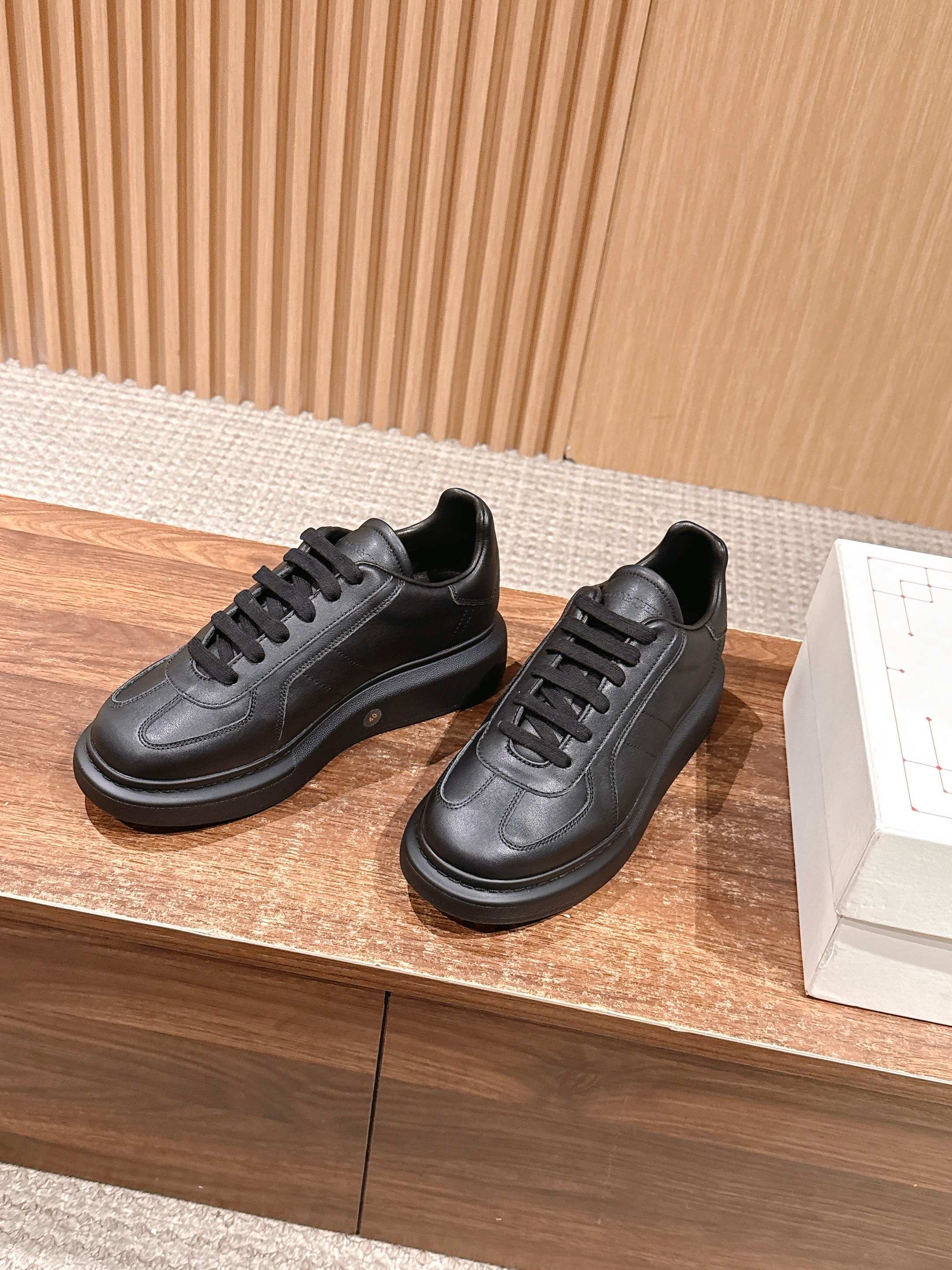 Black leather lace-up sneakers shown side by side on a display platform