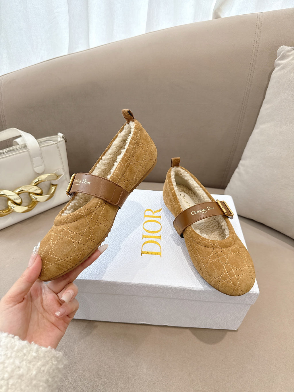 Tan suede flats with buckled strap and cream shearling lining, held by hand