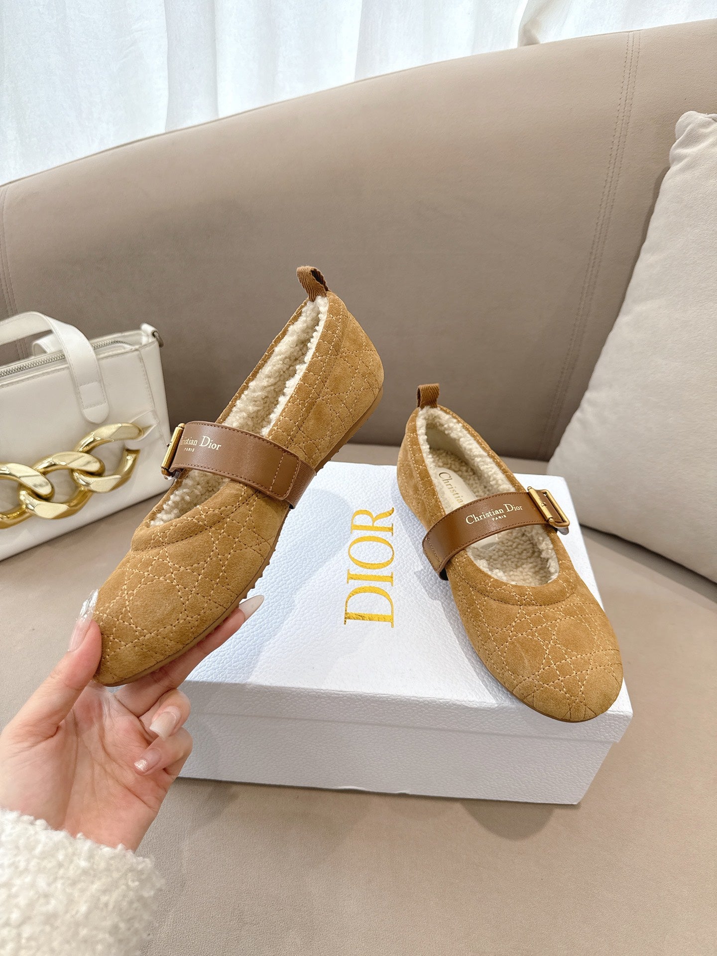 Tan suede flats with buckled strap and cream shearling lining, held by hand